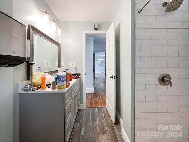 bathroom with vanity, hardwood / wood-style floors, a tile shower, and water heater