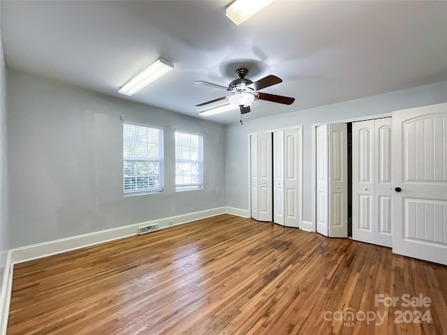 unfurnished bedroom with two closets, ceiling fan, and hardwood / wood-style floors