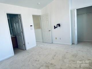 unfurnished bedroom featuring ensuite bathroom, lofted ceiling, light colored carpet, and a closet