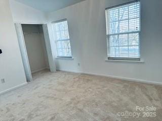 unfurnished bedroom with multiple windows, lofted ceiling, light colored carpet, and a closet