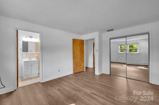 unfurnished bedroom with a closet, connected bathroom, light hardwood / wood-style floors, and sink