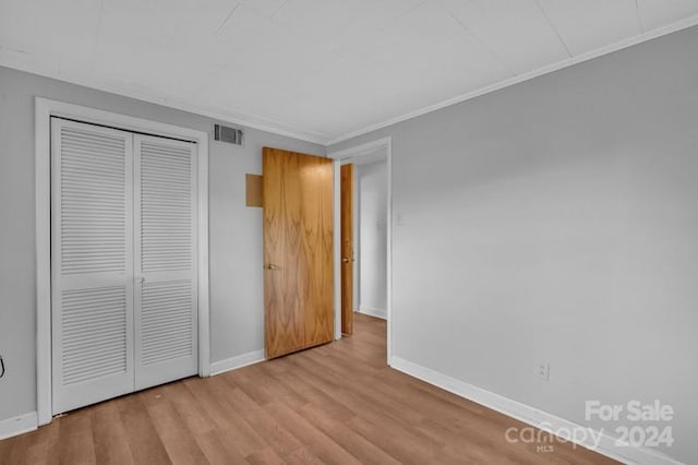 unfurnished bedroom featuring light wood-type flooring, crown molding, and a closet