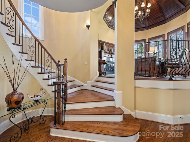 stairs with a high ceiling, crown molding, hardwood / wood-style floors, and a notable chandelier