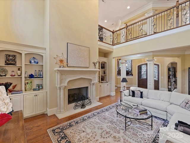 living room with built in shelves, decorative columns, a high ceiling, and light hardwood / wood-style flooring