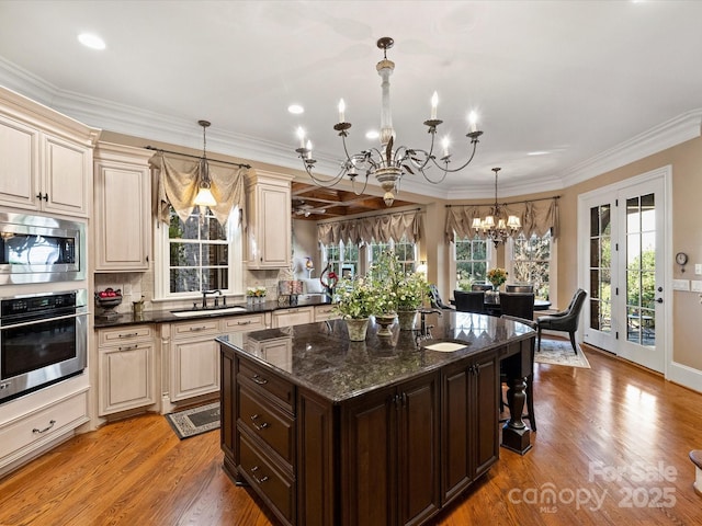 kitchen with cream cabinetry, stainless steel appliances, hanging light fixtures, dark brown cabinetry, and sink