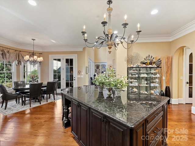 kitchen with dark stone countertops, hardwood / wood-style floors, pendant lighting, dark brown cabinets, and a chandelier