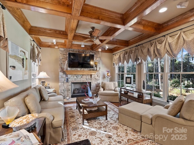 living room featuring hardwood / wood-style floors, beamed ceiling, a stone fireplace, ceiling fan, and coffered ceiling