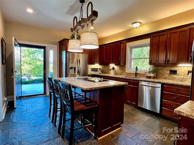 kitchen featuring a kitchen island, decorative light fixtures, backsplash, stainless steel appliances, and a breakfast bar area