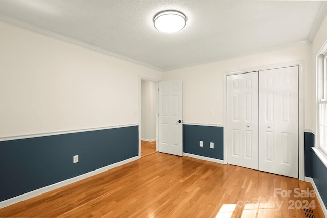 unfurnished bedroom featuring a textured ceiling, a closet, hardwood / wood-style flooring, ornamental molding, and multiple windows