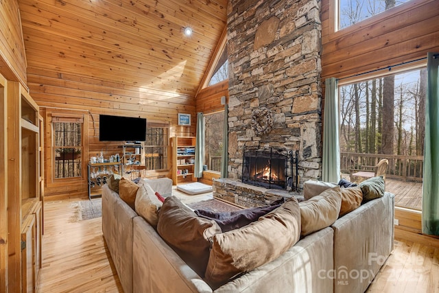 living room featuring wood walls, light wood-type flooring, wooden ceiling, a fireplace, and high vaulted ceiling