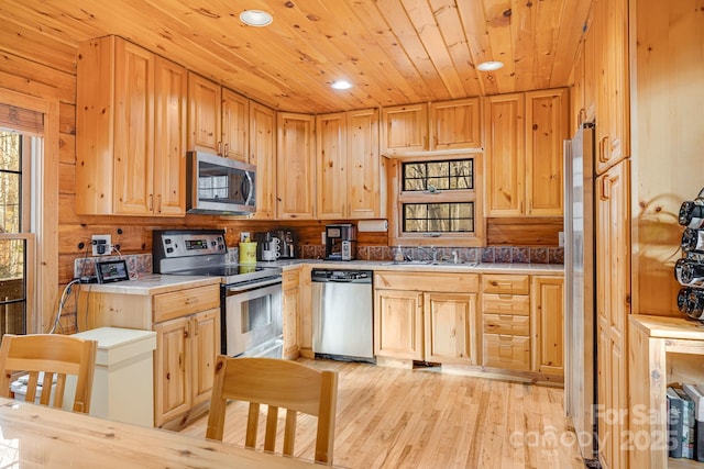 kitchen featuring light wood finished floors, tile countertops, wood ceiling, appliances with stainless steel finishes, and a sink