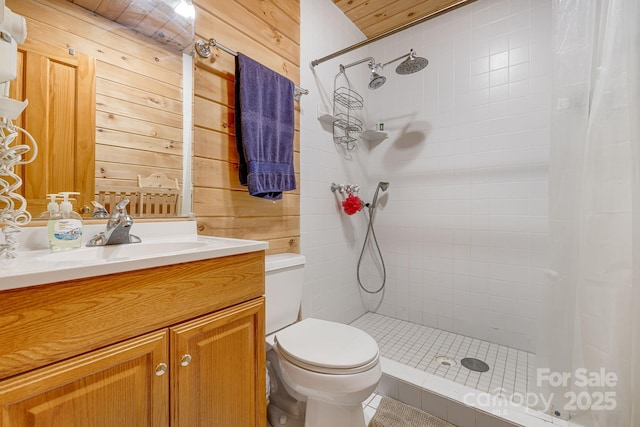 bathroom with wooden walls, tiled shower, toilet, and vanity