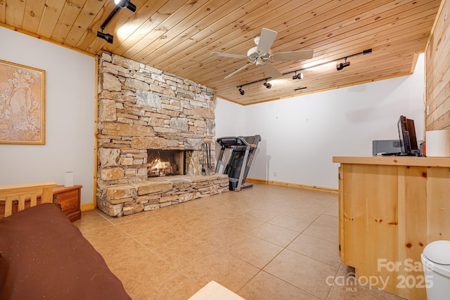tiled living room featuring a ceiling fan, baseboards, a stone fireplace, track lighting, and wood ceiling