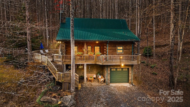 view of front facade with an attached garage, log exterior, driveway, and metal roof
