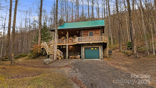 cabin with driveway, log siding, a chimney, a garage, and metal roof