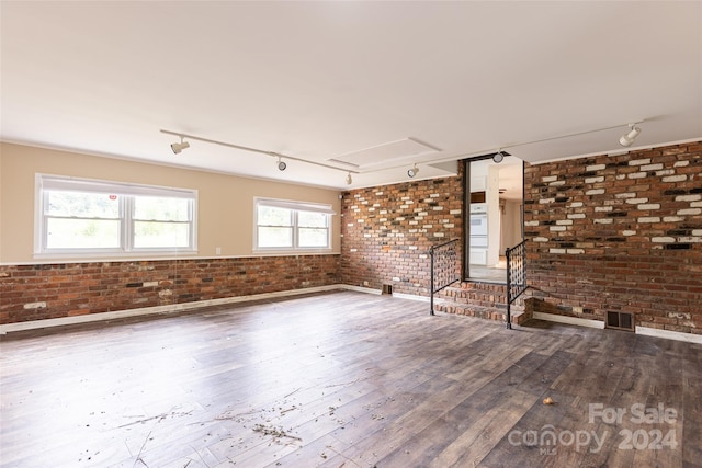 empty room featuring hardwood / wood-style floors, track lighting, and brick wall