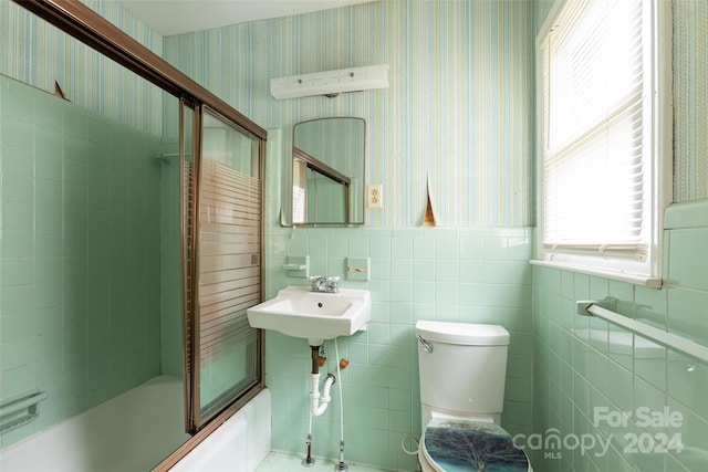 full bathroom featuring toilet, combined bath / shower with glass door, sink, and tile walls