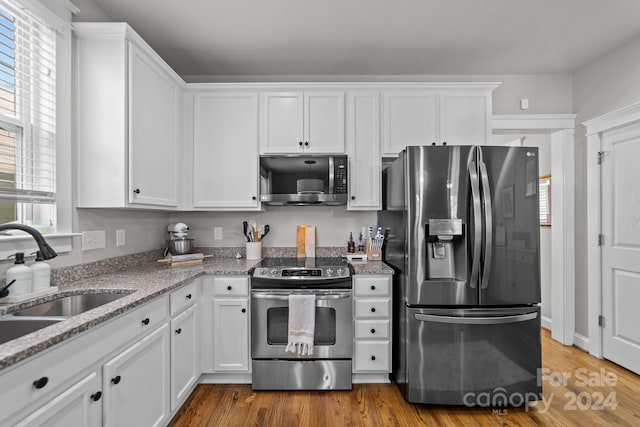 kitchen featuring wood-type flooring, light stone countertops, stainless steel appliances, and white cabinets