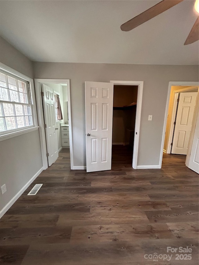 unfurnished bedroom featuring ensuite bathroom, a walk in closet, dark hardwood / wood-style floors, a closet, and ceiling fan