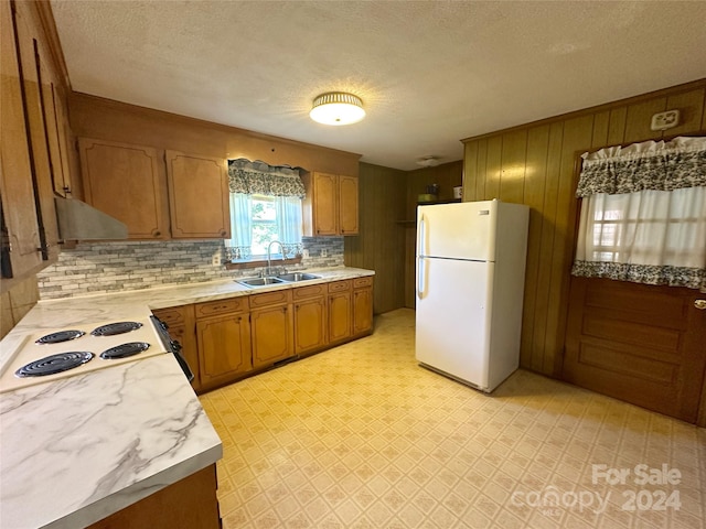 kitchen with a textured ceiling, white appliances, wooden walls, and sink