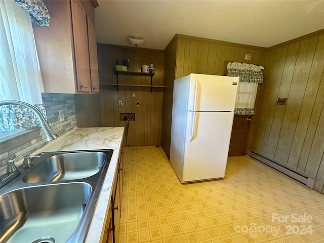 kitchen with white refrigerator, wood walls, sink, tasteful backsplash, and baseboard heating