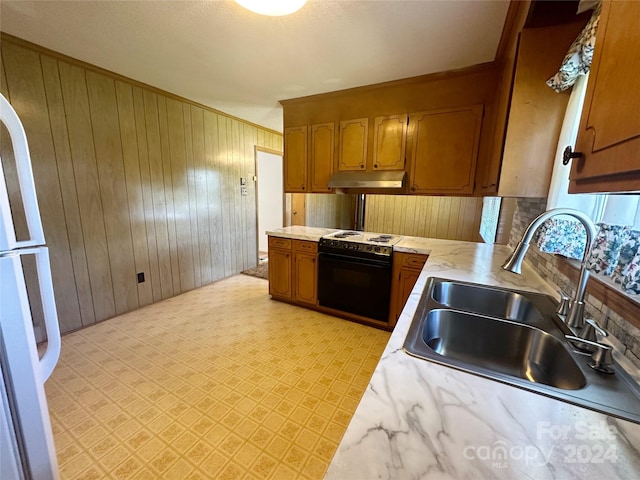 kitchen featuring decorative backsplash, wood walls, black range, and sink