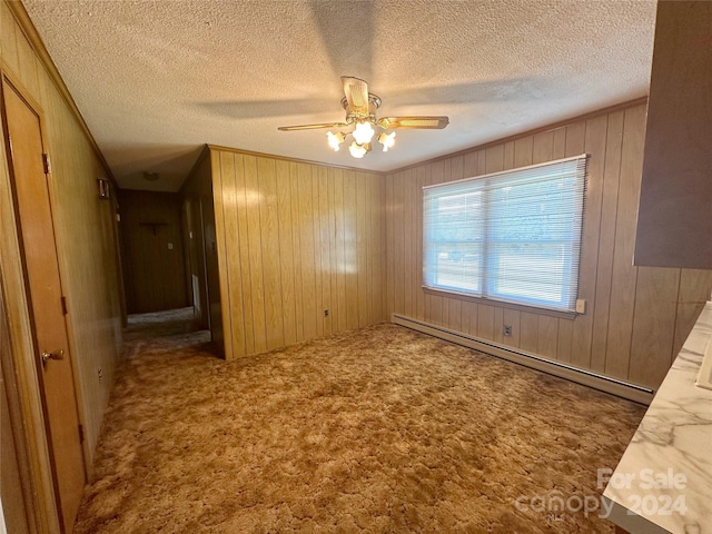 empty room with light carpet, wooden walls, a textured ceiling, and a baseboard radiator