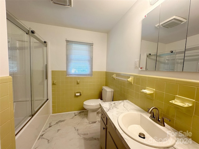 full bathroom with vanity, tile walls, toilet, and combined bath / shower with glass door