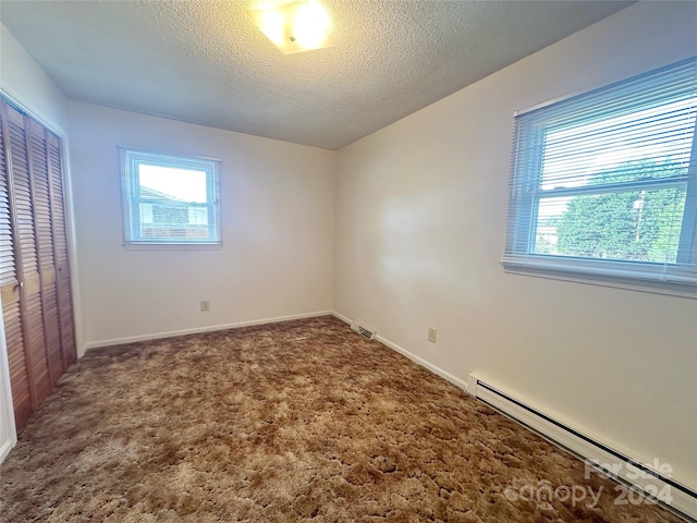 unfurnished room featuring a textured ceiling, dark colored carpet, and a baseboard heating unit