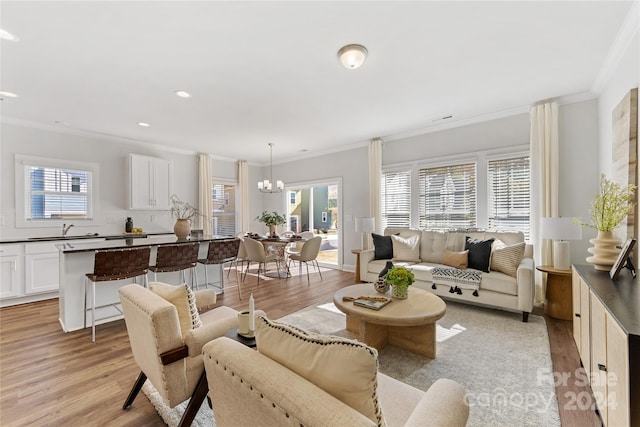 living room featuring sink, crown molding, light hardwood / wood-style flooring, and an inviting chandelier