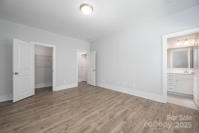 unfurnished bedroom with sink, light wood-type flooring, a walk in closet, ensuite bath, and a closet