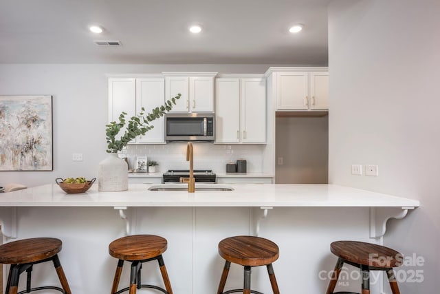 kitchen featuring stainless steel microwave, backsplash, visible vents, white cabinets, and a sink