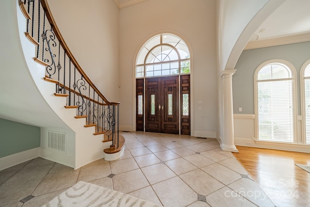 foyer entrance featuring light hardwood / wood-style flooring, crown molding, a high ceiling, and decorative columns