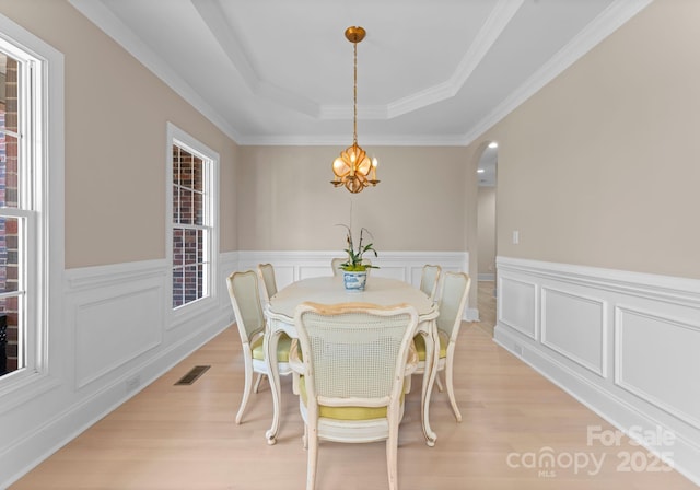 dining area with a chandelier, light wood-type flooring, a tray ceiling, and crown molding