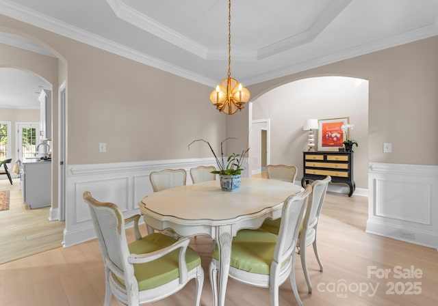 dining area with light wood-type flooring, a tray ceiling, an inviting chandelier, and ornamental molding