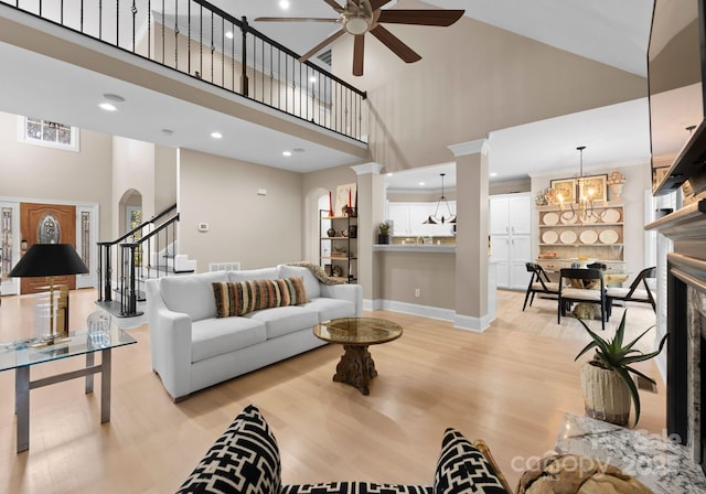 living room featuring ceiling fan with notable chandelier, light wood-type flooring, high vaulted ceiling, and a premium fireplace