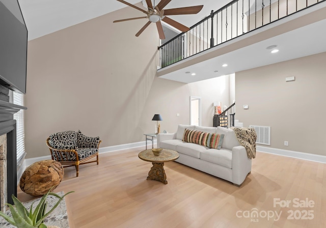 living room featuring a towering ceiling, light hardwood / wood-style floors, and ceiling fan