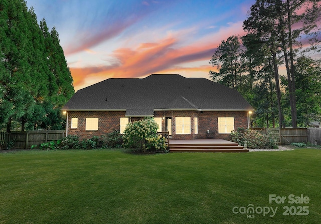 back house at dusk with a lawn and a wooden deck