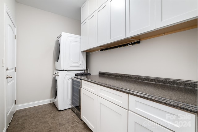 laundry area with stacked washing maching and dryer, cabinets, and dark tile patterned flooring