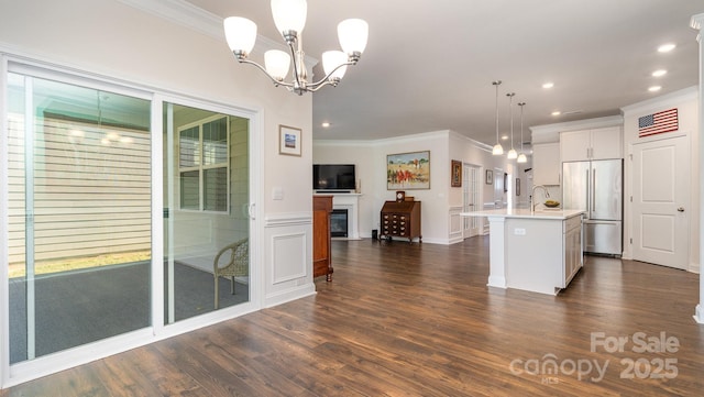 kitchen featuring white cabinetry, a chandelier, pendant lighting, a kitchen island with sink, and stainless steel built in fridge