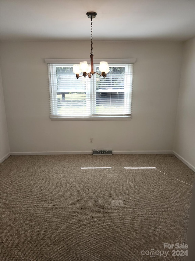 carpeted spare room featuring a chandelier and a wealth of natural light