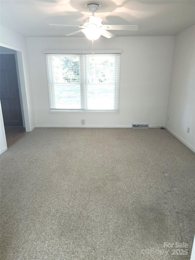 carpeted spare room with baseboards, visible vents, and a ceiling fan