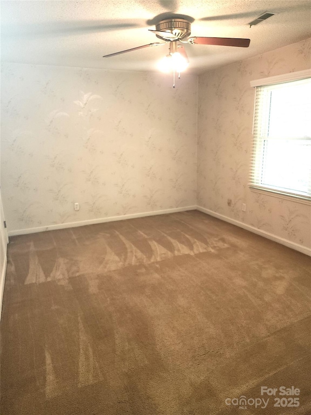 carpeted spare room with a ceiling fan, visible vents, and wallpapered walls