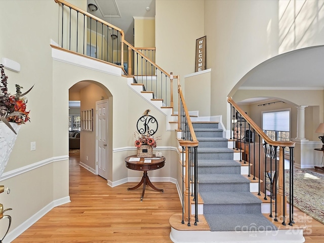 stairs with hardwood / wood-style flooring, ornate columns, crown molding, and a high ceiling