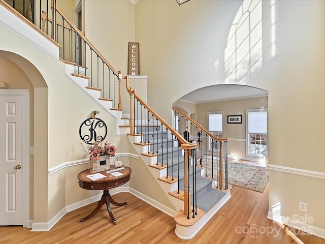 staircase featuring hardwood / wood-style flooring, crown molding, and a high ceiling