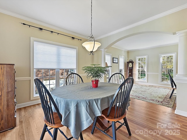 dining area with ornate columns, ornamental molding, and light hardwood / wood-style flooring