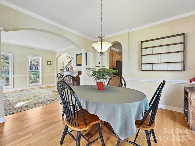 dining room with crown molding, light wood-type flooring, and ornate columns