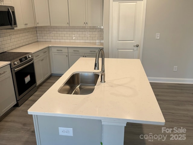 kitchen featuring a kitchen island with sink, sink, light stone counters, and appliances with stainless steel finishes