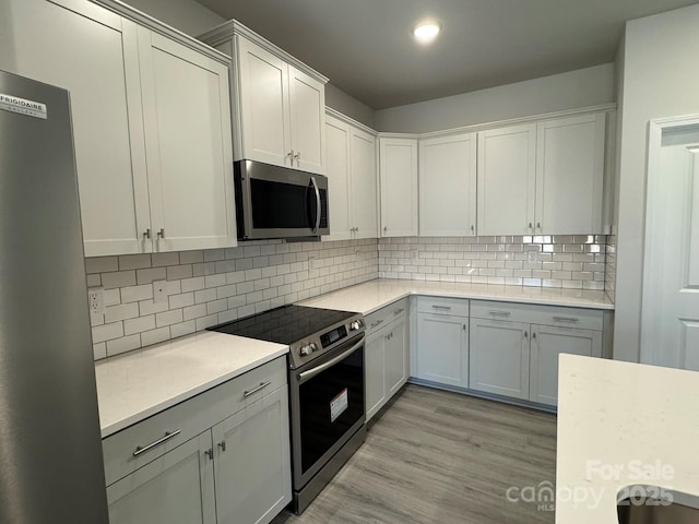 kitchen featuring stainless steel appliances, white cabinets, backsplash, and light wood-type flooring