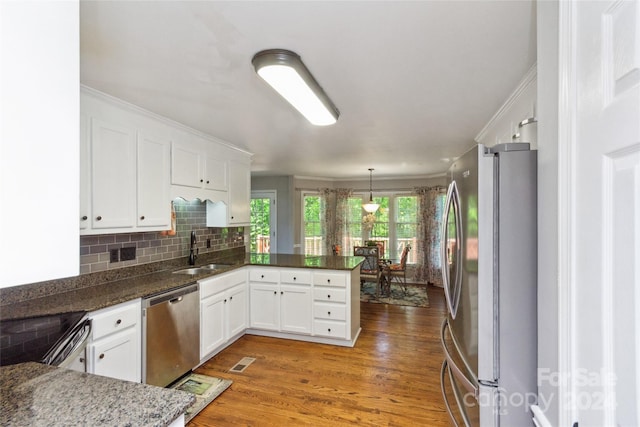 kitchen with dark hardwood / wood-style flooring, stainless steel appliances, kitchen peninsula, hanging light fixtures, and white cabinetry